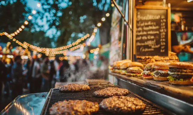 Hamburguesas humeantes en parrilla, listas para servir en un food truck. Un ejemplo de cómo montar un food truck exitoso con ambiente festivo.