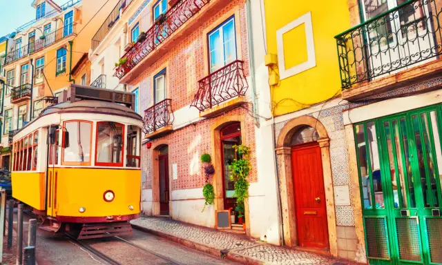 Gelber Straßenbahn fährt durch eine enge Gasse mit bunten Häusern. Ein typisches Bild der Umweltzone Lissabon.