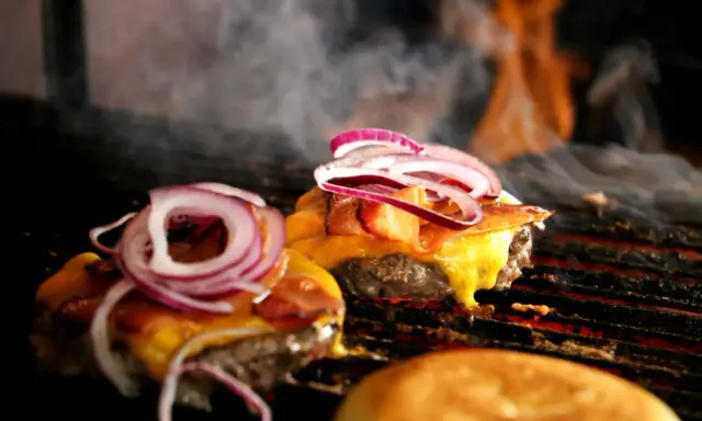 Pyszne burgery z grilla, z rozpływającym się serem i chrupiącym boczkiem, unoszą się w dymie.