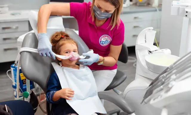 Dziecko w masce do sedacji wziewnej. Dentystka monitoruje stan pacjenta, minimalizując potencjalne skutki uboczne.