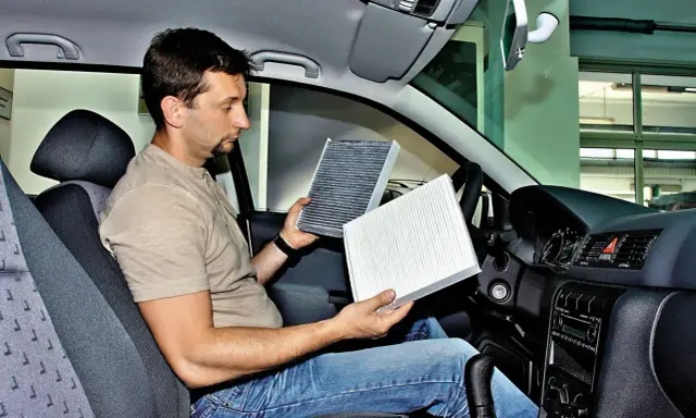 Mężczyzna w kabinie Renault Megane 3 porównuje stary i nowy filtr kabinowy, przygotowując się do jego wymiany.