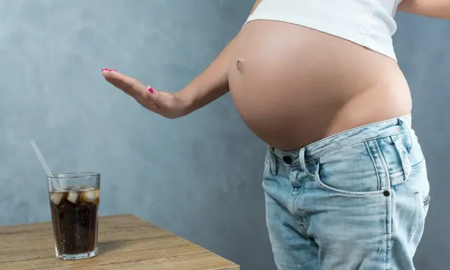 Schwanger und verzichtet auf Cola. Eine Hand weist ein Glas Cola mit Eis und Strohhalm ab.