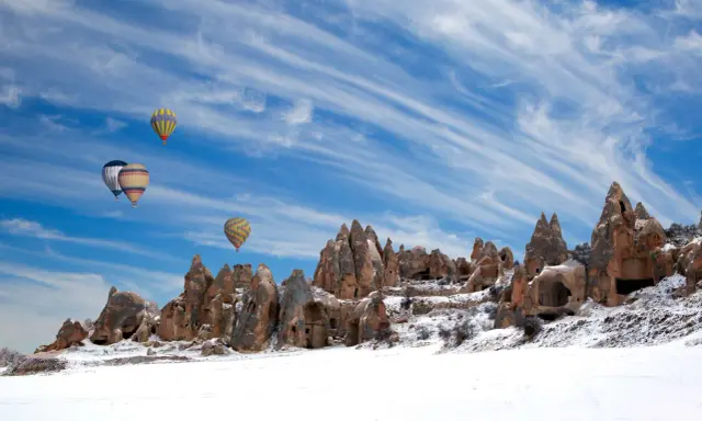 Balony unoszą się nad ośnieżonymi formacjami skalnymi w Kapadocji. Czy w Turcji pada śnieg? Tak, zimą krajobraz potrafi być bajkowy.