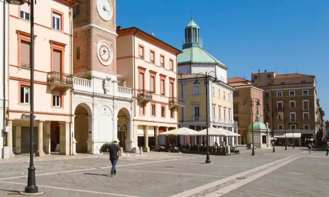 Passeggiata nella soleggiata piazza Tre Martiri a Rimini, con i suoi palazzi storici e il caratteristico orologio.