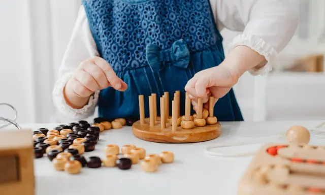 Niña con vestido azul jugando con cuentas de madera y un juego de encaje, parte de juegos para superar el mutismo selectivo.