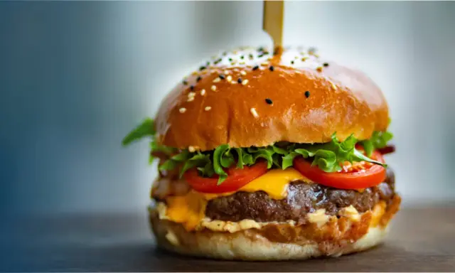 Un délicieux burger, avec sa brioche dorée, sa viande juteuse, son fromage fondant, sa laitue croquante et ses tomates fraîches. On se demande d'où vient le burger, ce classique indémodable.