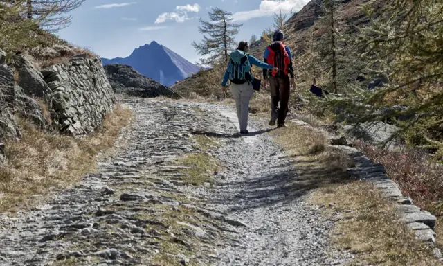 Escursionisti su sentiero sassoso nel Val di Susa, con montagne sullo sfondo.