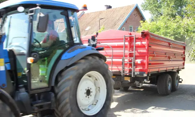 Rolnik z prawem jazdy na ciągnik prowadzi maszynę z czerwoną przyczepą.