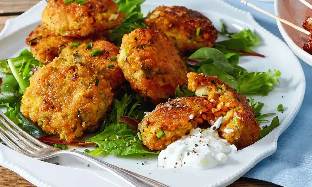 Knusprige Linsenbällchen mit Zucchini und Kräutern, serviert als fingerfood vegetarisch mit Dip auf Salatbett.
