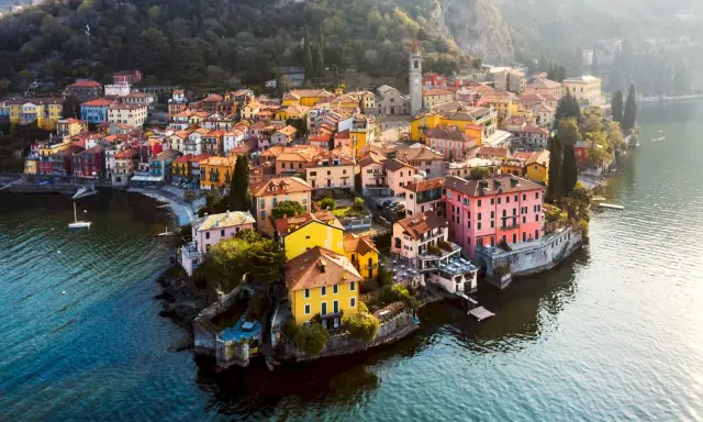 Färgstark by vid en sjö i norra Italien, med hus i gult, rosa och orange som klättrar uppför en sluttning.