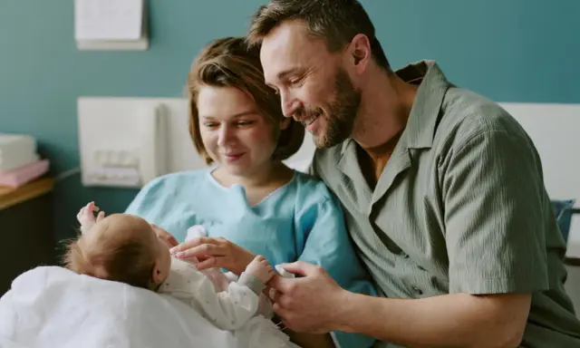 Szczęśliwi rodzice z noworodkiem w szpitalu. Dowiadują się o świadczenia po urodzeniu dziecka.