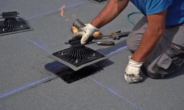 Instalador aplica calor con soplete para fijar tela asfáltica a base de techo, asegurando impermeabilización.