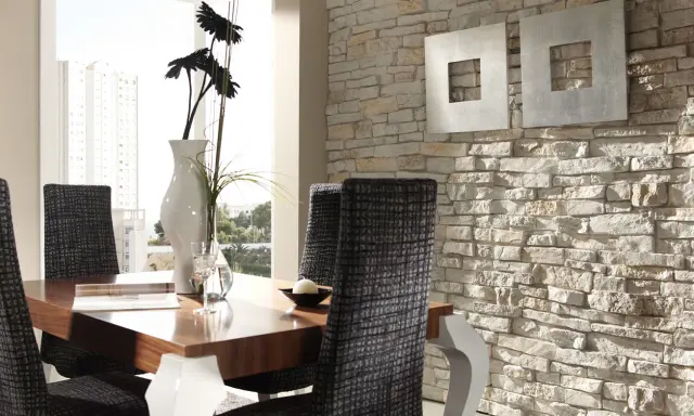 Comedor moderno con mesa de madera, sillas tapizadas y una pared con distintos tipos de revestimientos de piedra.