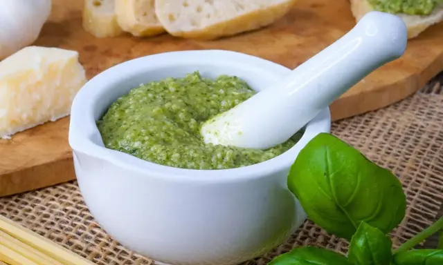 Frisches Basilikum-Pesto im Mörser, bereit zum Genießen. Dazu Brot, Parmesan und Pasta – so einfach ist basilikum pesto selber machen.
