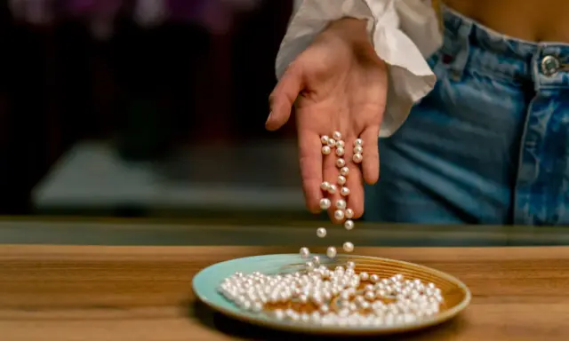Main d'une personne versant des perles de culture sur une assiette. Apprenez comment nettoyer les perles de culture pour qu'elles brillent.
