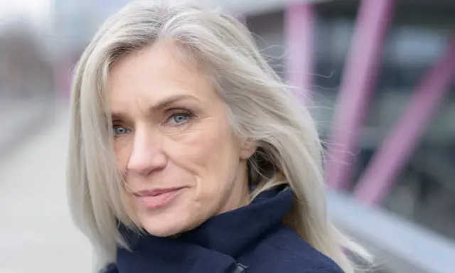 Donna con capelli bianchi e occhi azzurri, indossa un cappotto blu scuro. Un esempio di come vestirsi con i capelli bianchi.