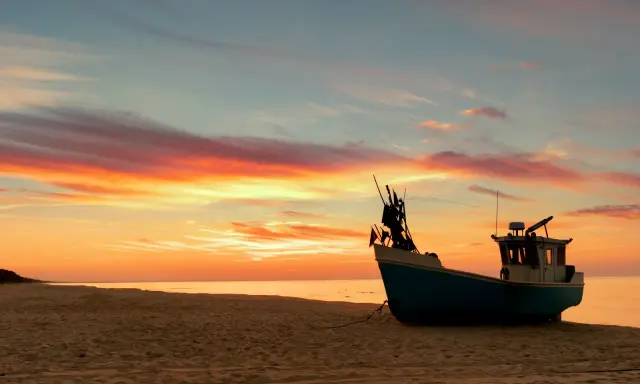 Zachód słońca na plaży Wyspy Sobieszewskiej. Łódź rybacka na piasku, malownicze chmury. Atrakcje przyrodnicze.