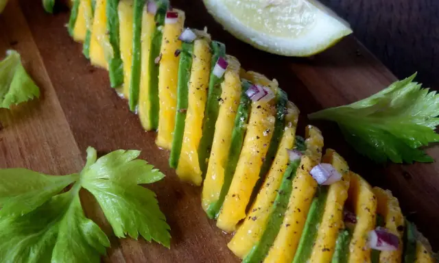 Une belle recette avocat et mangue, assaisonnée d'oignon rouge et de poivre, sur une planche en bois.