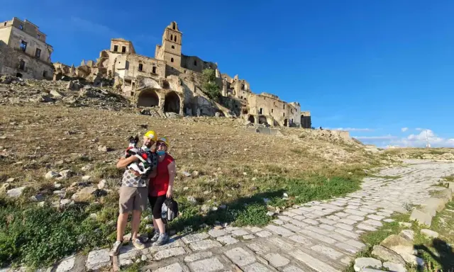 Coppia con cane visita le suggestive rovine di Craco vecchia, un borgo fantasma sotto un cielo azzurro.