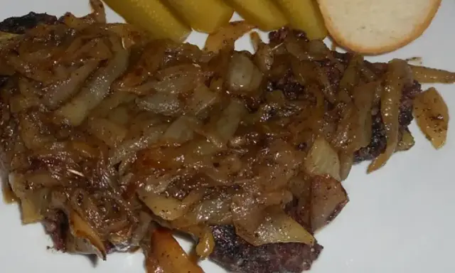 Pyszna kaszanka z patelni, duszona z cebulką, podana z ogórkiem kiszonym i kromką chleba.