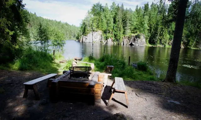 En mysig eldstad med bänkar vid en stilla sjö, omgiven av grönskande skog. Ett perfekt utflyktsmål i Dalarna för avkoppling.