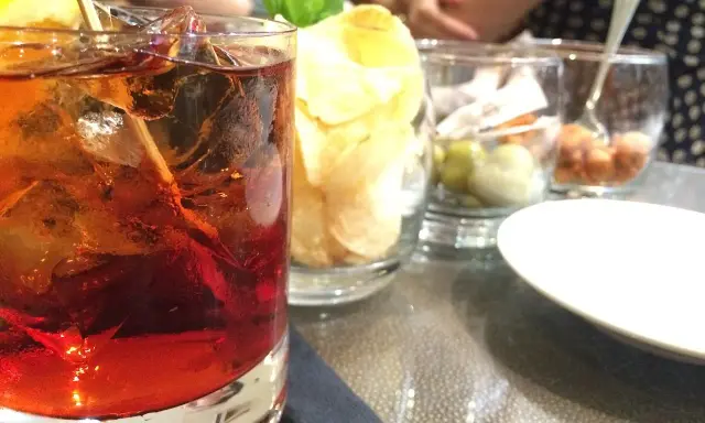 Czerwony drink z lodem i cytryną, obok chipsy i oliwki. Idealny aperitif, jak zrobic martini?