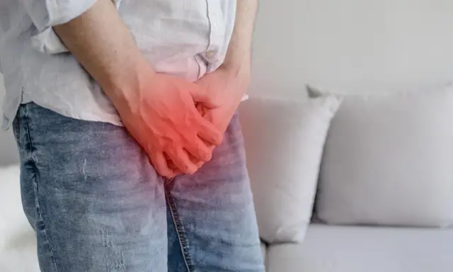 Mężczyzna trzyma się za krocze, gdzie widoczny jest czerwony obszar bólu, sugerujący chorobę Peyroniego.