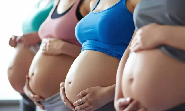 Fyra gravida kvinnor står sida vid sida och håller sina magar. En av dem, andfådd gravid, ler.
