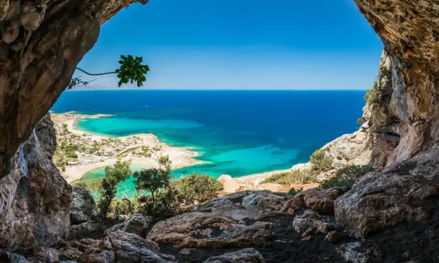 Widok z jaskini na turkusowe morze i plażę. Idealna kreta pogoda w kwietniu, słońce i błękitne niebo.