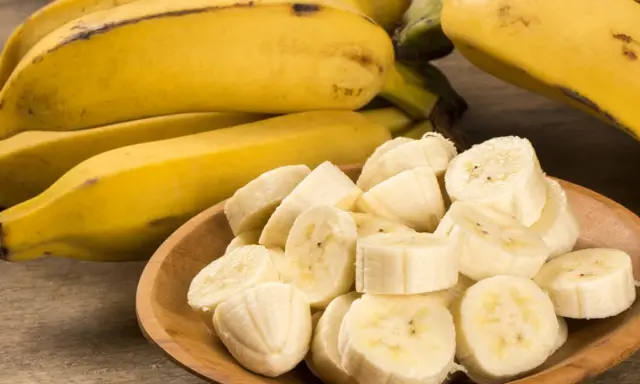 Kawałki bananów w drewnianej misce obok całych owoców. Te żółte banany, bogate w potas, są świetne dla zdrowia nerek.