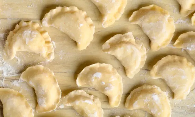 Surowe pierogi z farszem na pierogi ruskie, ułożone na drewnianym blacie, posypane mąką.