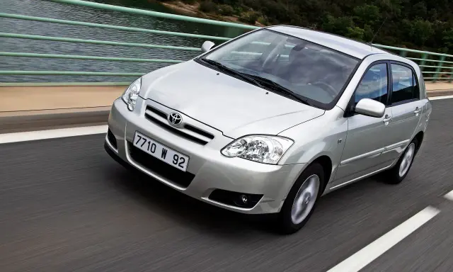 Srebrna Toyota Corolla 2004 na moście, z widokiem na wodę i las.