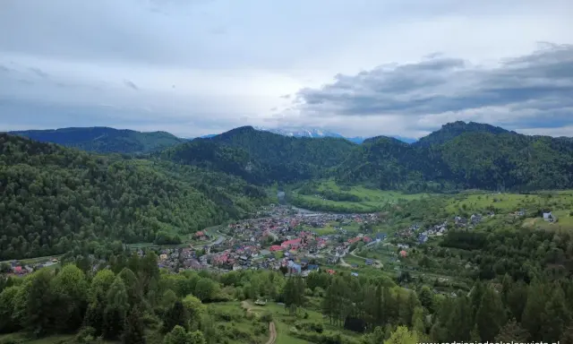 Widok na malowniczą dolinę z miasteczkiem Szczawnica. W oddali góry, a na pierwszym planie zielone wzgórza. To idealne miejsce na odkrywanie szczawnickich atrakcji.