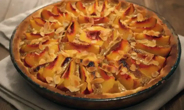 Tarte aux pêches amande, une gourmandise dorée aux fruits fondants et éclats d'amandes effilées, prête à être dégustée.