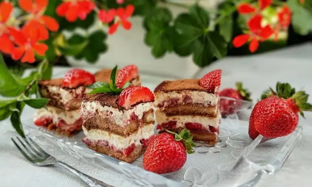 Pyszne tiramisu truskawkowe z warstwami biszkoptu, kremu i świeżych truskawek, posypane kakao i udekorowane owocami.