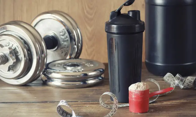 Pesas, batidora y cuchara con proteína en polvo. Ideal para saber cuándo tomar batido de proteínas y optimizar tu entrenamiento.