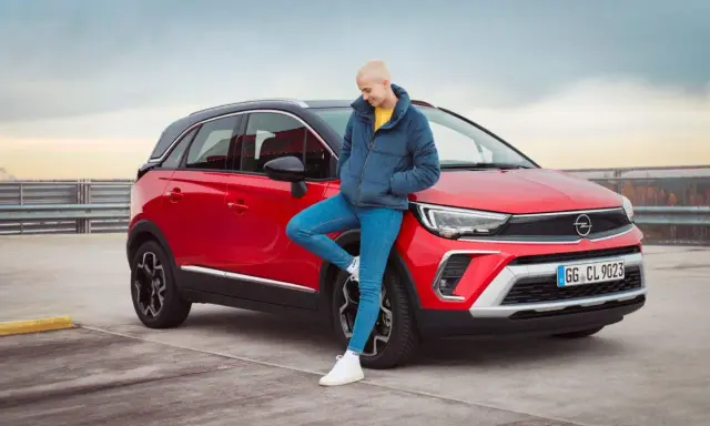 Joven apoyada en un Opel Crossland X rojo. Evita problemas con la correa de distribución de tu Opel Crossland X con un mantenimiento adecuado.