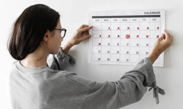 Mujer revisa calendario, marcando días. No me baja la regla y no estoy embarazada, preocupación en su rostro.