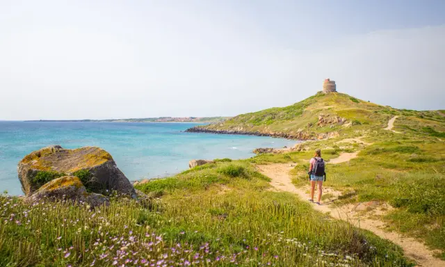 Sentiero panoramico per un tour Sardegna 7 giorni, con torre antica e mare turchese.