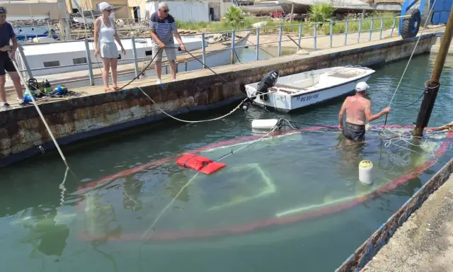 Un bateau accidenté est partiellement submergé dans un port. Des personnes sur le quai tentent de gérer la situation.