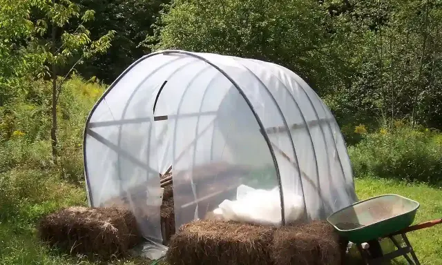 Un invernadero listo para el huerto de verano, con fardos de paja y carretilla a los lados.