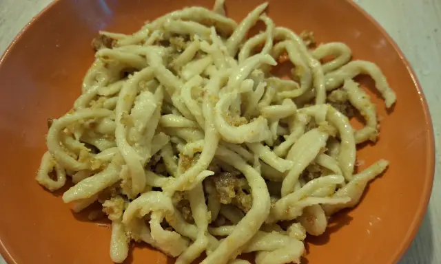 Pici fatti in casa con un saporito sugo per i pici, serviti in un piatto arancione.