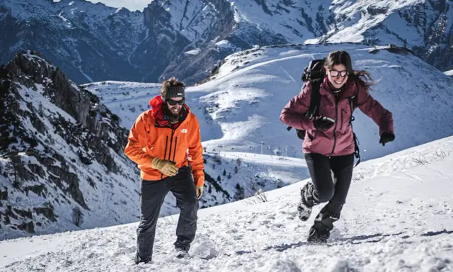 Coppia in montagna con abbigliamento da neve, godendosi l'estate in un paesaggio innevato.
