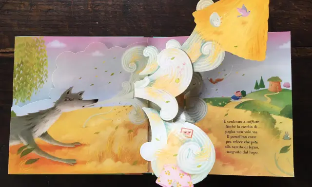 Libri pop-up più belli: un lupo soffia su una casetta di paglia, mentre un maialino corre verso una casetta di legno.