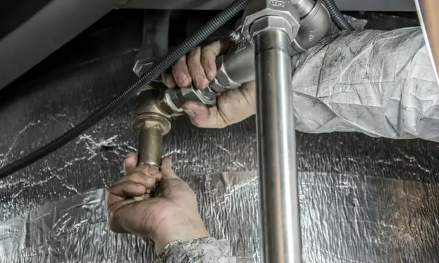 Instalator dokręca złączkę, by zapobiec dostawaniu się powietrza w rurach od wody.