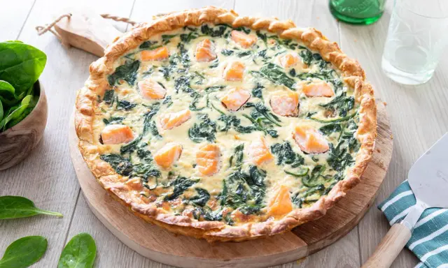 Une délicieuse quiche saumon épinard, dorée et garnie de morceaux de poisson et de légumes verts, prête à être dégustée.