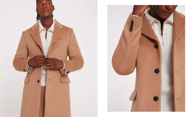 A man models a stylish camel coat, perfect for wearing with a suit. The coat features dark buttons and a classic lapel.