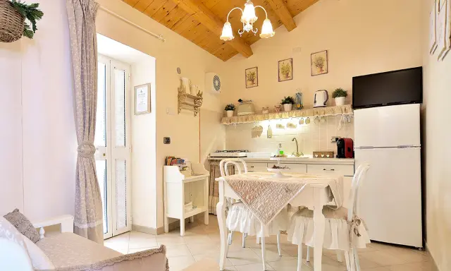 Cuisine et coin repas dans un style shabby chic, avec des meubles blancs, des textiles doux et des poutres apparentes.
