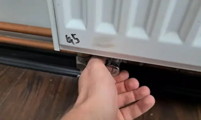 Ręka reguluje zawór grzejnika aluminiowego, próbując wyeliminować szum w grzejnikach aluminiowych.