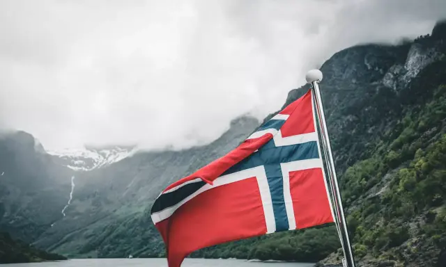 Norweska flaga na tle fiordu. Marzenie o pracy w Norwegii staje się rzeczywistością.